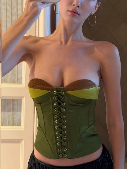 A woman wearing a structured strapless corset top in olive green with brown side panels and lime green underbust bands, shown in a mirror selfie.
